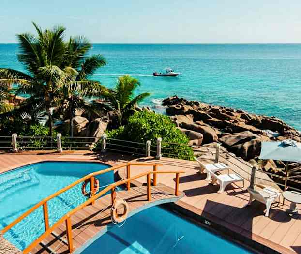 Bassengområde med utsikt over havet, omgitt av palmer og steiner. (AI-generert tekst)