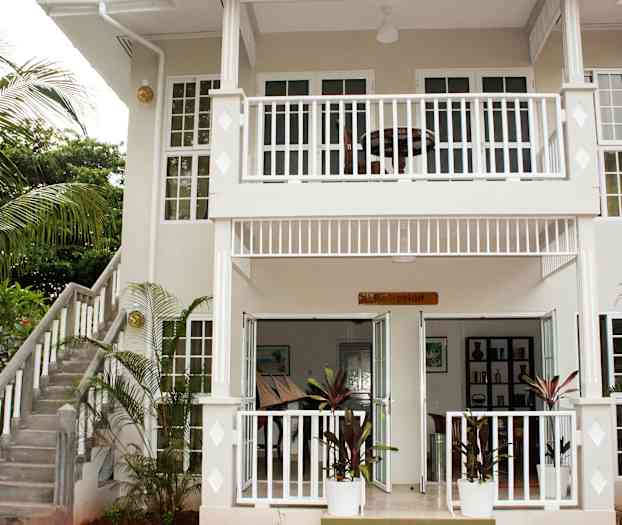 Inngangen til en toetasjes bygning med et skilt ved inngangen som sier "Resepsjon" og en omgivende hage. (AI-generert tekst)