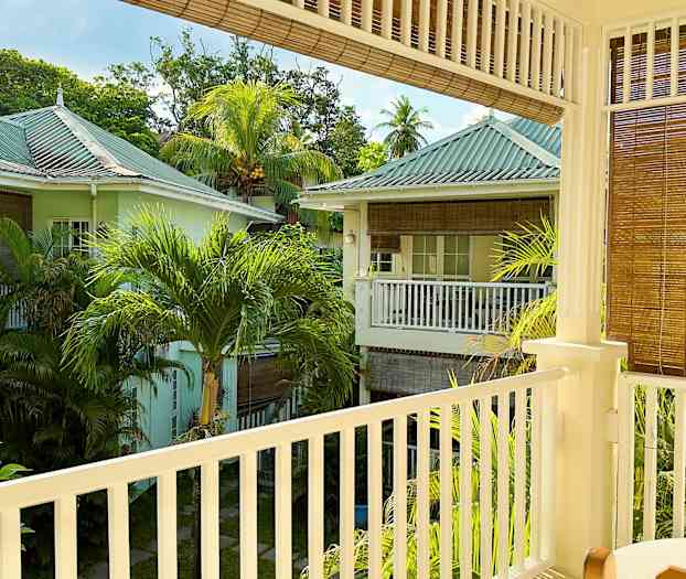 En utsikt fra en balkong som viser et frodig område med pastellfargede hus og palmetrær. (AI-generert tekst)