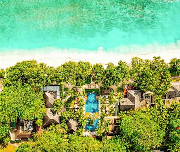 Luftfoto av et hotell ved en strand med basseng, omgitt av grøntområder. (AI-generert tekst)