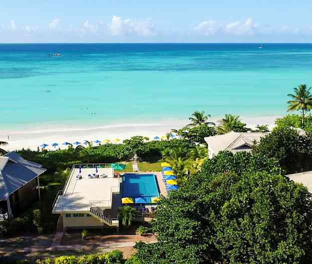 Et feriehotell ved en strand med turkist vann og omliggende grøntområder. (AI-generert tekst)
