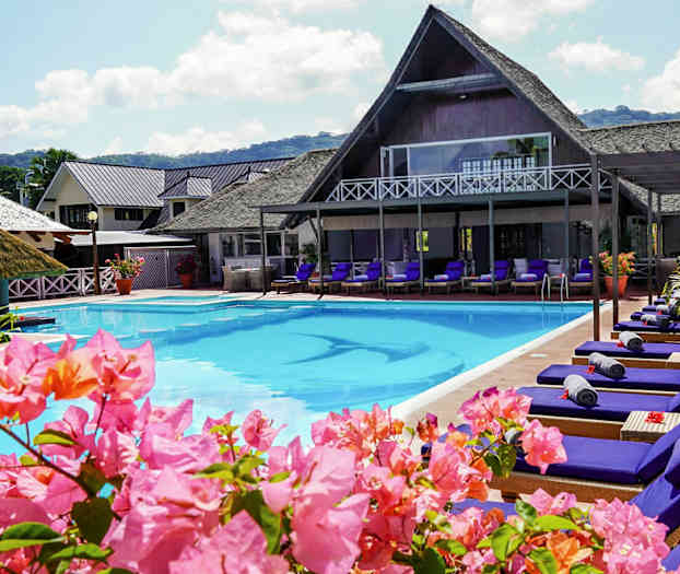 Bassengområde med solsenger og blomster, bygninger i bakgrunnen. (AI-generert tekst)