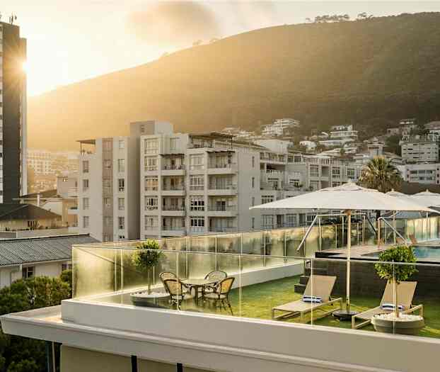 Takterrasse med solsenger, bord og parasoller, basseng i bakgrunnen og en bymiljø med frodige åser. (AI-generert tekst)