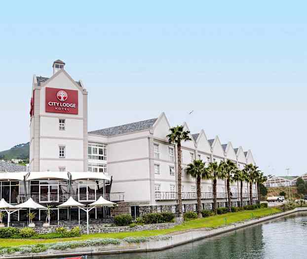 Et hotell med lys fasade, kantet av palmer og en kanal foran. (AI-generert tekst)