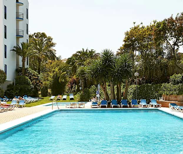 Et basseng omgitt av solsenger og trær. (AI-generert tekst)