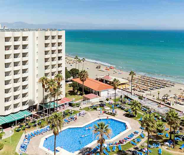 Et hotell med basseng og solsenger nær en sandstrand ved havet. (AI-generert tekst)