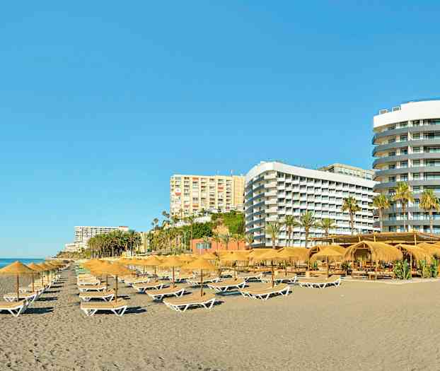 En strand med solsenger og parasoller, omgitt av flere hotellbygninger. (AI-generert tekst)