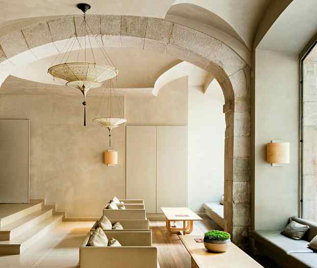 Et elegant innredet rom med hvelvbuer, moderne møbler og store vinduer som vender mot en gate. (AI-generert tekst)