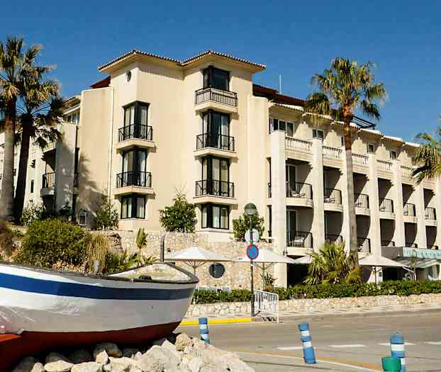 En bygning med balkonger og palmer foran, samt en båt på land. (AI-generert tekst)