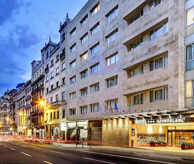 En bygateg med et hotell kalt Montblanc er synlig på høyre side, med flere fasadebygg og kveldsbelysning. (AI-generert tekst)