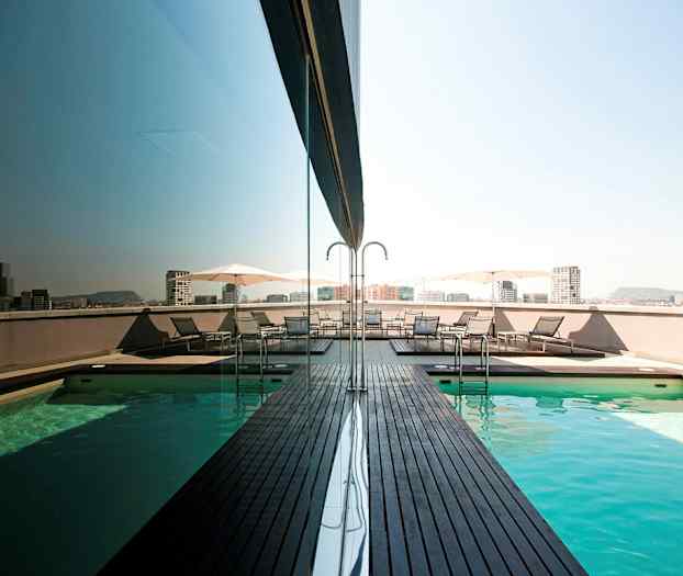 Et takbasseng med treplattformer og solsenger ved siden av. Byen vises i bakgrunnen. (AI-generert tekst)