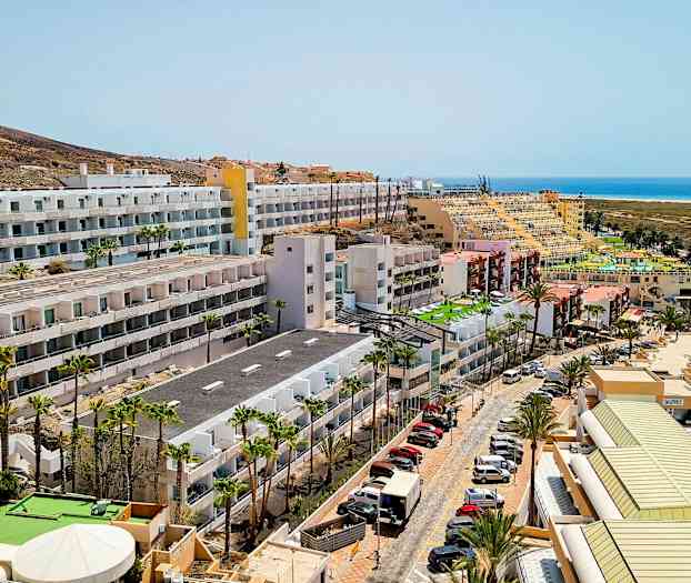 Hotellbygninger nær havet med parkerte biler og palmer. (AI-generert tekst)