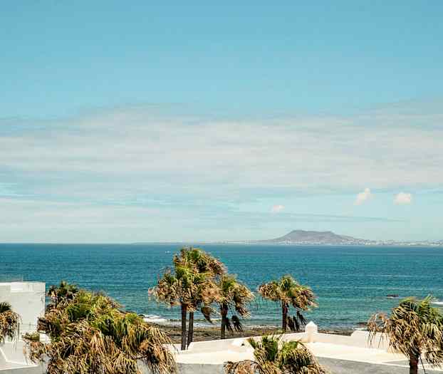 Utsikt over havet med palmer i forgrunnen og et fjell i bakgrunnen. (AI-generert tekst)