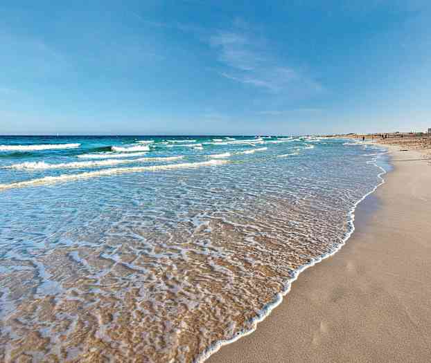 En sandstrand med myke bølger som skyller inn, under en klar blå himmel. (AI-generert tekst)