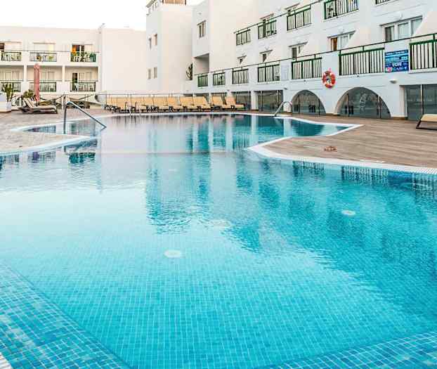 Utendørs svømmebasseng på et feriested med solsenger og hvite bygninger i bakgrunnen. (AI-generert tekst)