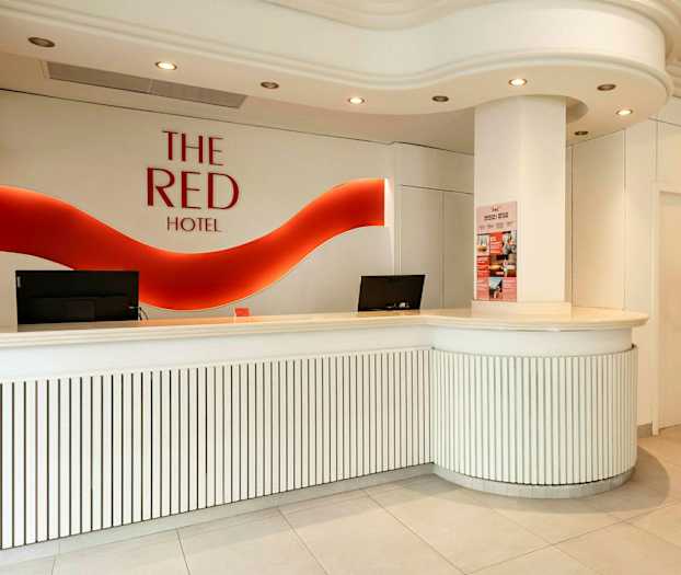 Hotellresepsjon med hvit innredning og rød logo på veggen. (AI-generert tekst)