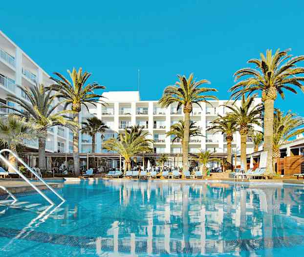 Bildet viser et basseng foran et hotell med flere etasjer, omgitt av palmer under en klarblå himmel. (AI-generert tekst)