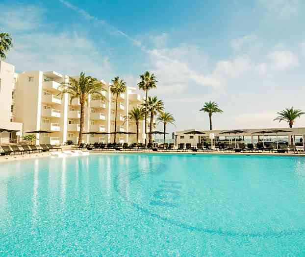 Et stort basseng foran et moderne hotell omgitt av palmetrær under en blå himmel. (AI-generert tekst)