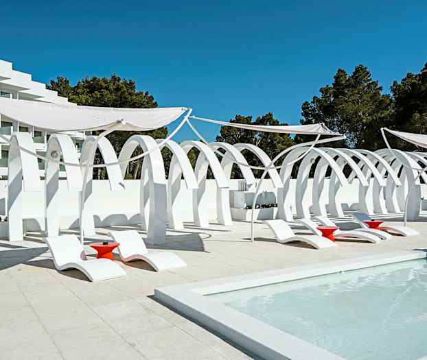 Hvit arkitektur med buer, samt solsenger og røde bord ved et basseng. (AI-generert tekst)