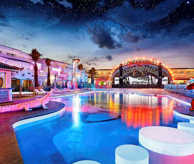 Et utendørsbasseng ved et opplyst hotellområde under nattehimmelen. (AI-generert tekst)