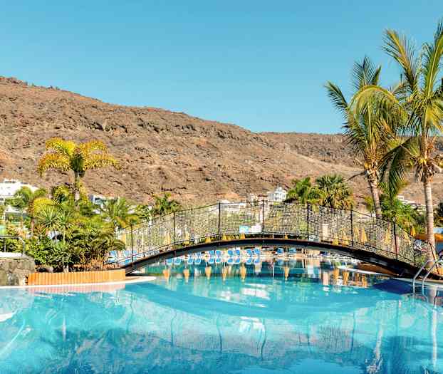 Et basseng med en bro og palmer omkranset av fjell. (AI-generert tekst)