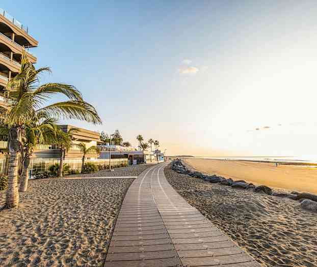 En strandpromenade ved en sandstrand med palmer og bygninger. (AI-generert tekst)