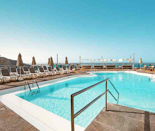 Bassengområde med solsenger og parasoller samt utsikt over havet. (AI-generert tekst)