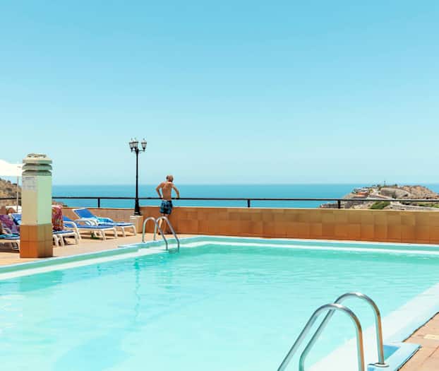 Utendørs basseng med havutsikt, solsenger og parasoller. (AI-generert tekst)