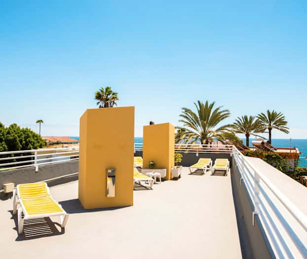 En takterrasse med solsenger og utsikt over palmer og havet. (AI-generert tekst)