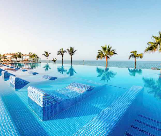 Et infinitybasseng med utsikt over havet og omkringliggende palmer. (AI-generert tekst)