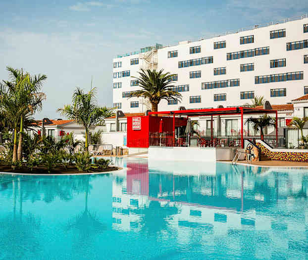 Et hotellområde med et stort basseng, omgitt av palmer og bygninger med hvite fasader. (AI-generert tekst)