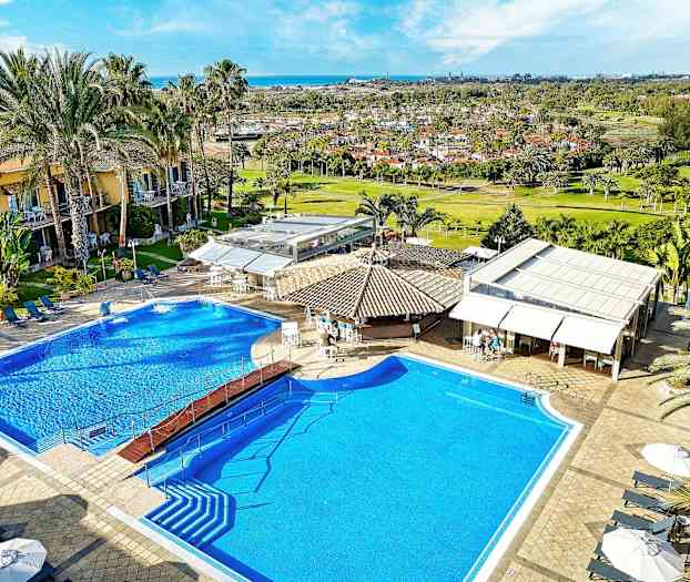 Bilde av et hotellbasseng med solsenger, parasoller og omkringliggende bygninger. (AI-generert tekst)