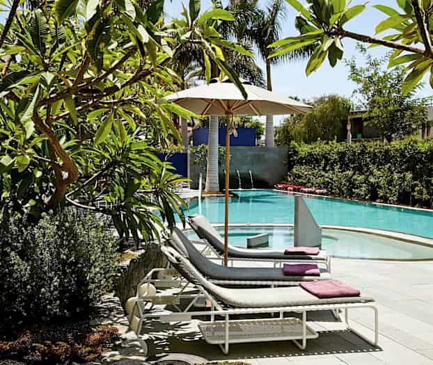 Solstoler ved et basseng med parasoll og frodige omgivelser. (AI-generert tekst)