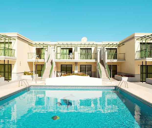 Et basseng foran en bygning med balkonger og grønne detaljer. (AI-generert tekst)