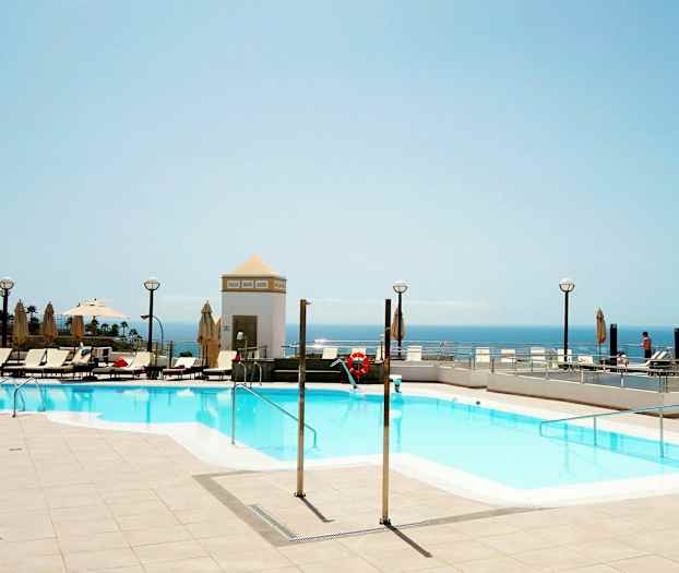 Utendørsbasseng med solsenger og utsikt over havet. (AI-generert tekst)