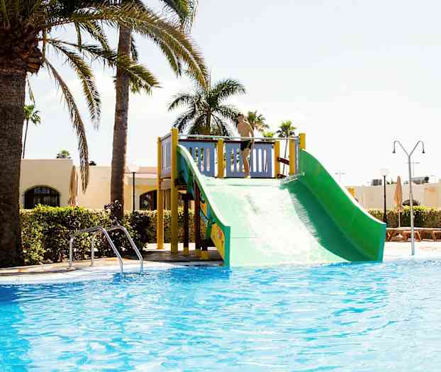 En vannsklie ved et basseng, omgitt av palmer og bygninger. (AI-generert tekst)