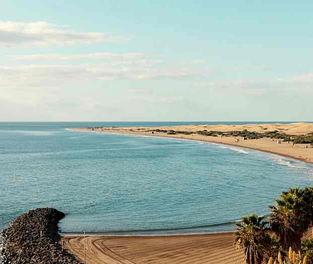 Utsikt over en strand med sanddyner, havet og en smal steinmolo. (AI-generert tekst)