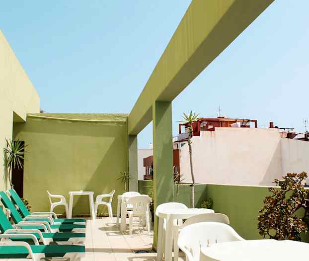 Terrasse med solsenger og bord, omgitt av grønne vegger. (AI-generert tekst)