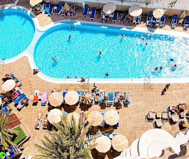 Et utendørs basseng med solsenger og parasoller ved siden av. (AI-generert tekst)