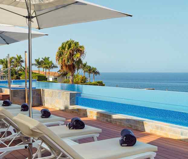 Solstoler og parasoller ved et infinity-basseng med utsikt over havet. (AI-generert tekst)