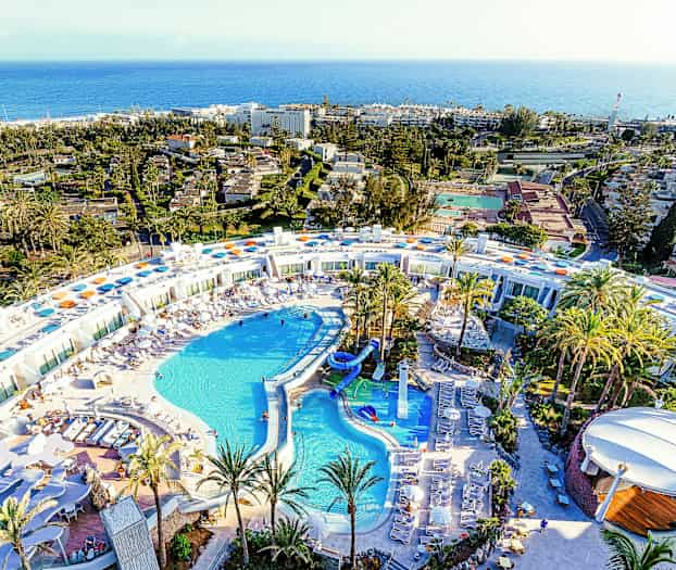 Flyfoto av et stort feriested med bassengområde og omgitt av palmer. (AI-generert tekst)