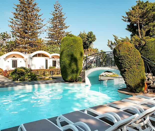 Utendørsbasseng med romslig område, solsenger og en liten bro i hagen. (AI-generert tekst)