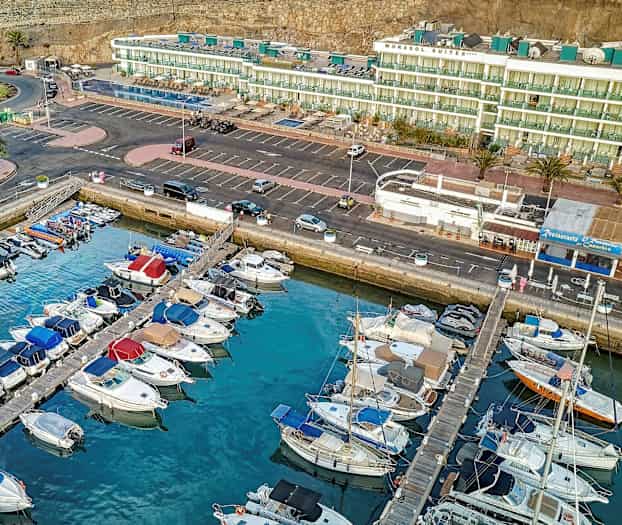 Luftfoto av en marina med parkerte båter foran bygninger og parkeringsplasser. (AI-generert tekst)