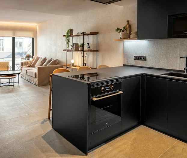 Bilde av en moderne stue og kjøkken med stilren innredning. Viser en grå kjøkkenøy og en sofa i bakgrunnen. (AI-generert tekst)