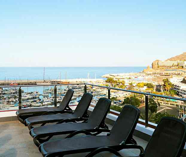 Bilde av en terrasse med solsenger som har utsikt over en marina og havet. (AI-generert tekst)