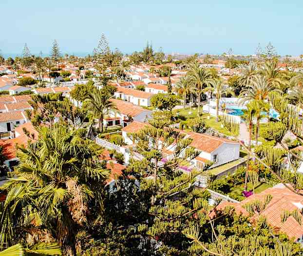 Utsikt over et feriested med hvite hus, røde tak og grønne trær rundt omkring. (AI-generert tekst)