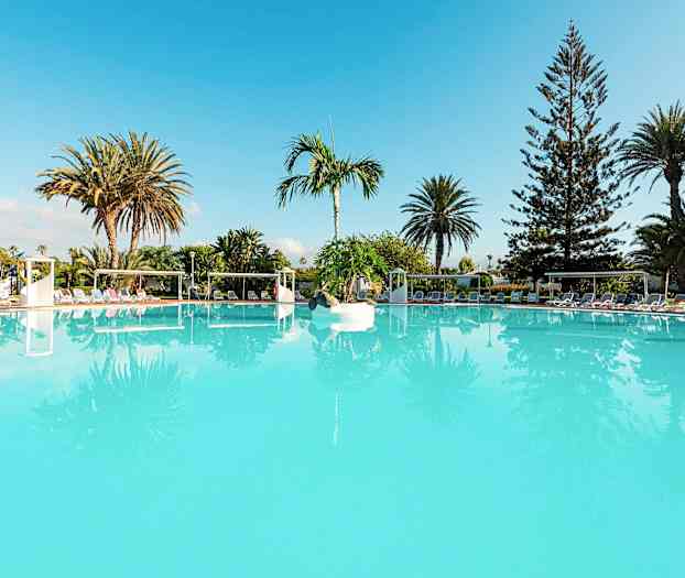 Et stort turkis svømmebasseng omgitt av solsenger og palmetrær. (AI-generert tekst)