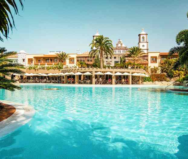 Et stort basseng foran en bygning med palmer og parasoller. (AI-generert tekst)