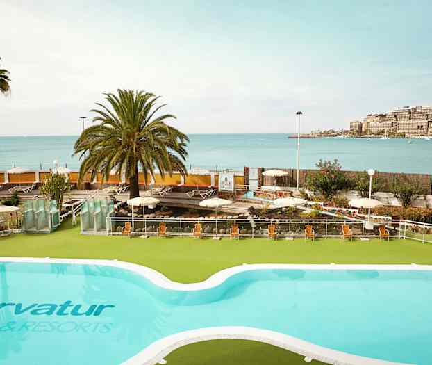 Et basseng med utsikt over havet og en solrik terrasse med solsenger. (AI-generert tekst)