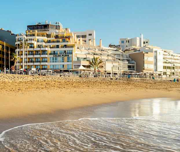 En sandstrand ved havet med bygninger i bakgrunnen. (AI-generert tekst)